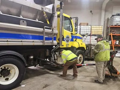 Two patrol workers doing maintenance on a snow plow